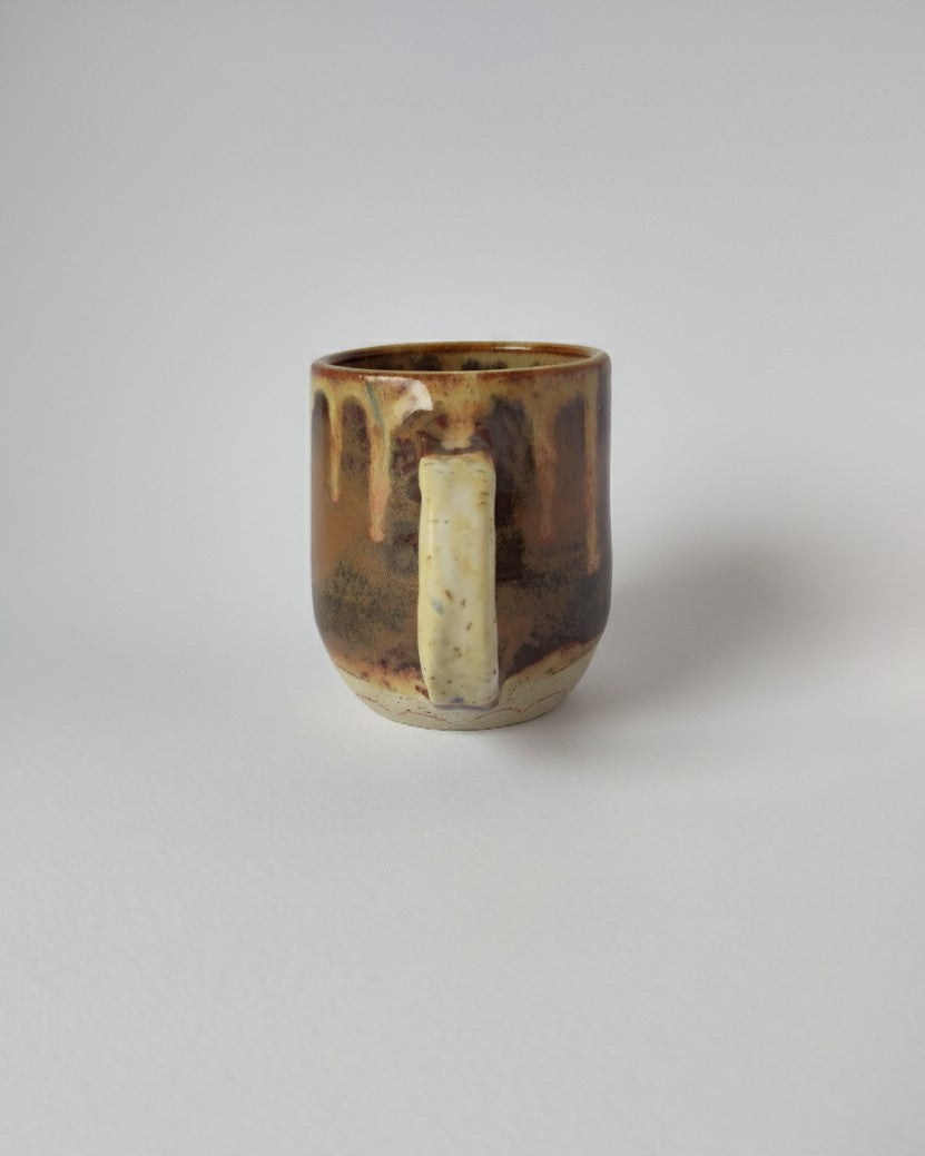 Ceramic mug with brown and beige glaze on a light gray background