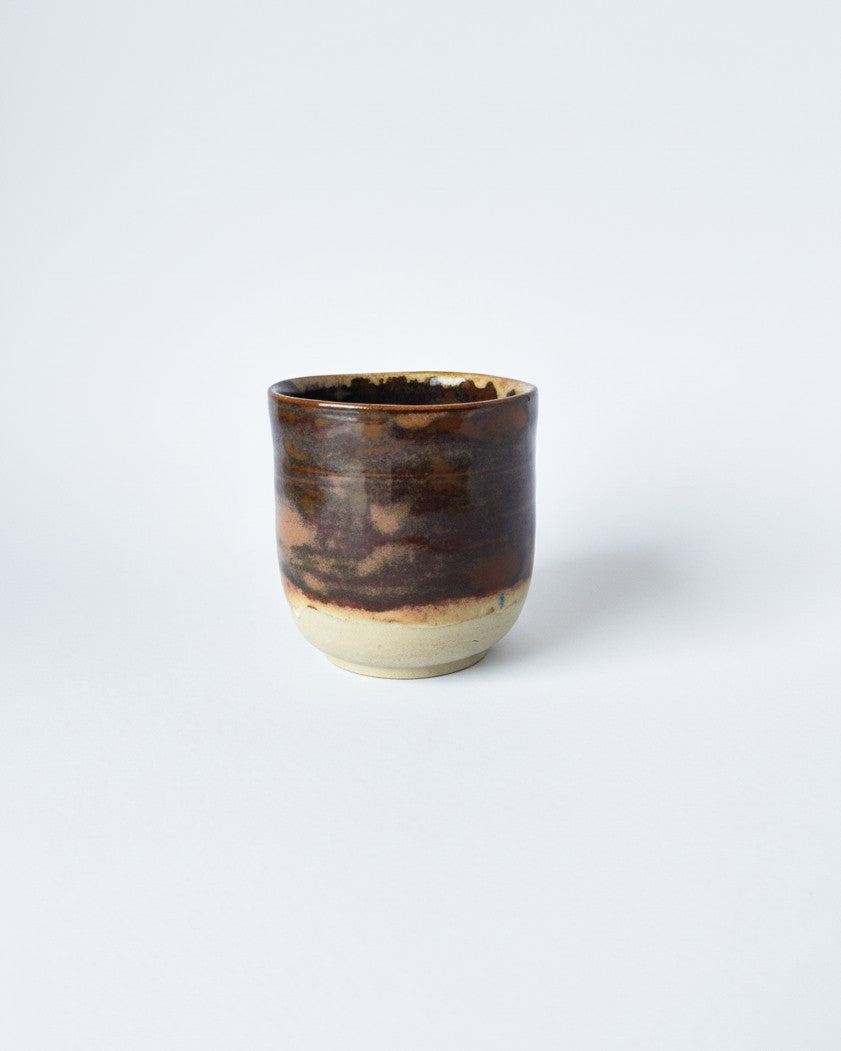 Ceramic cup with brown and beige glaze on a white background